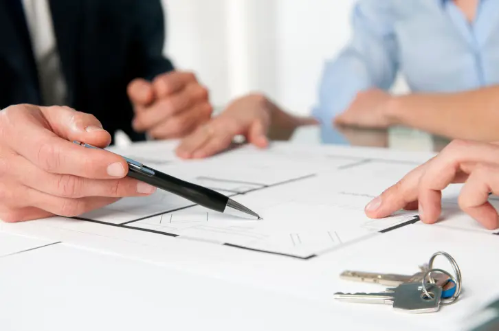 People at a table looking at a floorplan with keys and someone holding a pen